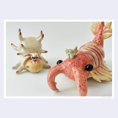 2 ceramic pieces of large crustaceans standing next to one another. One is akin to a shrimp and the other is akin to a snail. They have small characters sitting atop their backs.