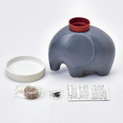 Product display, showing a shallow, white ceramic dish, a gray modern designed elephant with an empty pot on its head, a wrapped disc of peat, seeds and instructions. 