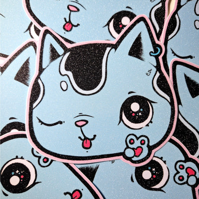 Glittery sticker of a blue cartoon cat's head, with black spots. It winks and throws up a peace sign with its paw, smiling with a tongue out expression. 