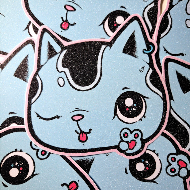 Glittery sticker of a blue cartoon cat's head, with black spots. It winks and throws up a peace sign with its paw, smiling with a tongue out expression. 