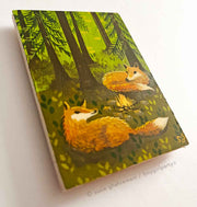 Painting of 2 foxes, laying in front of a small campfire in the middle of a forest with tall trees. Background is bright green, with the foreground mostly browns.