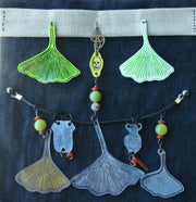 Collage on black fabric of colored plastic pieces, mostly upside down gingko leaves with beads and charms.