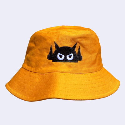 Goldenrod bucket hat with a black embroidered logo of a robot head, with white angry eyes.