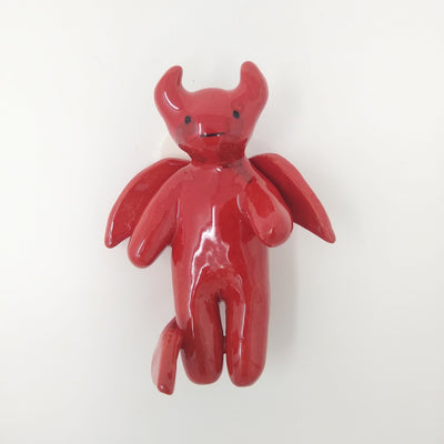 Ceramic sculpture of a red cute cartoon devil, with mostly sooth body features and small horns and wings.