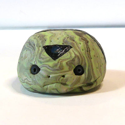 Small marbled green clay sculpture of a frog with a very pudgy body and a black triangle on its forehead. It sits with its arms and legs pulled in.