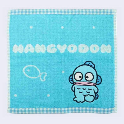 Turquoise blue square face towel with bubble text that reads "Hangyodon" with the Sanrio character, a blue fish person, under posing next to a simple fish drawing. Outline is blue gingham pattern.