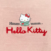 Dusky pink long sleeve shirt with a graphic in the center of Hello Kitty reading a book. Around her says "Hmmmmm.." with half the text on one side and the other half on the other. Below is a red yarn embroidered element spelling out "Hello Kitty".