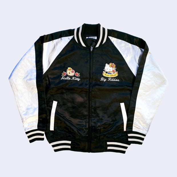 Sukajan style bomber jacket with a black semi shiny body with ivory colored sleeves and color accents. Front has 2 small graphics on the lapel, a skull with a straw hat and roses with "Hello Kitty" written underneath in cursive. Opposite of it is Hello Kitty with a rose patterned yellow bow and a banner that reads "Rose Skull".