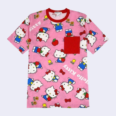 Pink t-shirt with a repeating all over pattern of Hello Kitty, standing and sitting with flowers and apples. "Hello Kitty" is written in white font throughout the pattern. Shirt has a red collar and shirt pocket.