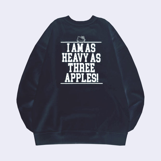 Back view of a navy blue sweatshirt with white text in all caps reading "I am as heavy as three apples!" with a small line art graphic of Hello Kitty's head appearing along the top of the text block.