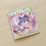 Booklet cover for "Cutelife Zine Issue 2" - featuring an illustration of a girl with purple braided hair and large anime style sparkling eyes, winking with her tongue out. She holds a greatsword over her shoulder, which is white aside from a floral pattern. She has a tattoo that reads "Cute Life" within a doily heart.