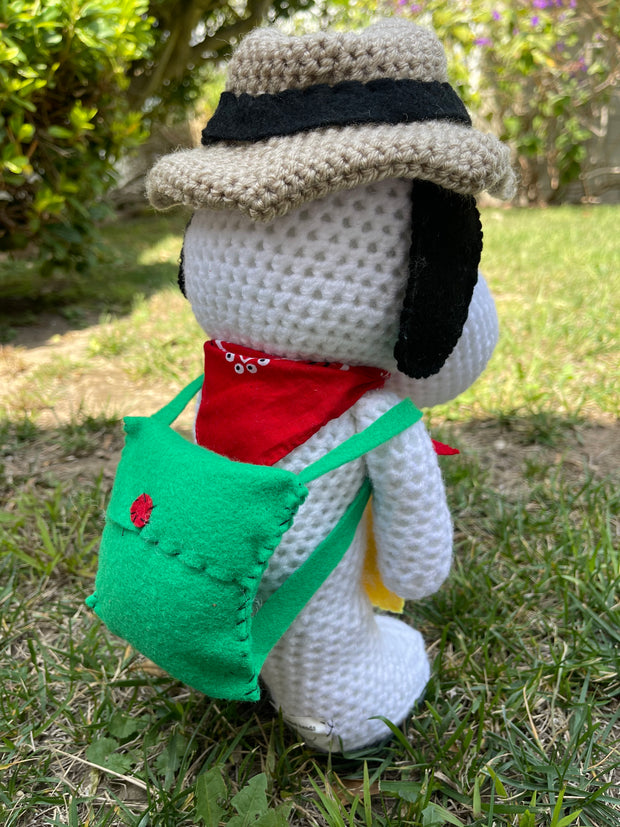 Crocheted plush doll of Snoopy with a brown outdoors hat, a red scarf and a green backpack. He holds a yellow felt map of Sawtelle.