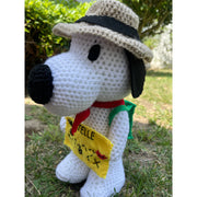 Crocheted plush doll of Snoopy with a brown outdoors hat, a red scarf and a green backpack. He holds a yellow felt map of Sawtelle.