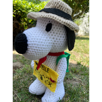 Crocheted plush doll of Snoopy with a brown outdoors hat, a red scarf and a green backpack. He holds a yellow felt map of Sawtelle.