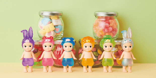 6 figures of Kewpie babies, nude aside from different colored translucent shorts and hood hats of various animals such as: rabbit, bear, pig, sheep and dog. They pose in front of jars of candy.