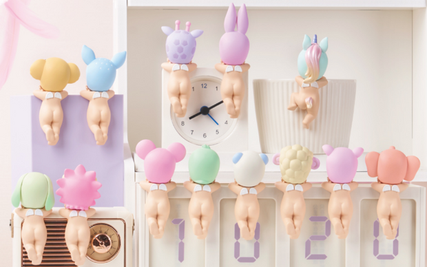 All 12 figure options from Sonny Angel Dreaming Hipper Series. Every figure is of a Kewpie baby facing away so only its nude body is showing with its legs crossed and a small pair of angel wings on its back. All of them wear a hood hat of a pastel colored animal.