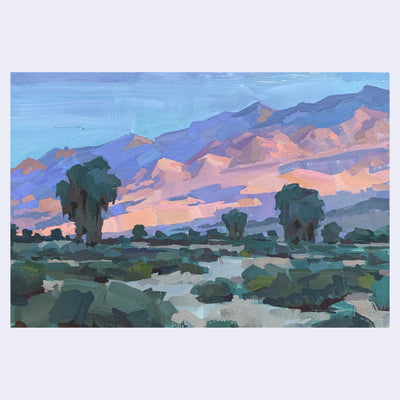 Plein air painting of a desert landscape with many green bushes and trees. The mountains in the back are lit by the setting sun, making them a pink and purple.