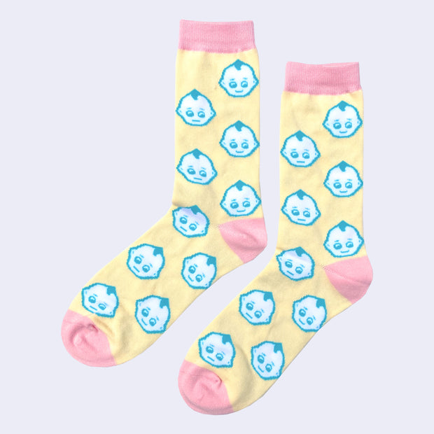 Pair of light yellow socks with pink color accents around the toe, ankle and top. They have a repeating pattern of Kewpie heads, white with a blue outline.