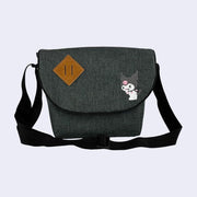 Dark gray messenger bag with an embroidery of Kuromi, looking back over her shoulder and snickering. The back has an extendable strap handle and a brown leather off tilt square patch.