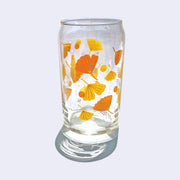 Glass cup with a wrap around graphic of orange and yellow gingko leaves and thin purple flowers. Back side.