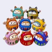 Arrangement of 8 different designs of a cat dressed as a daruma doll, with their arms raised up and varying expressions of joy or contentment. Colors are all different.