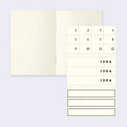 Interior of a notebook with blank ivory colored paper and a small sticker set of numbers and "idea" spaces.