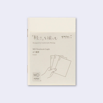 Cream colored blank cover journal within packaging with a cream insert that has Japanese writing and an illustration of a hand holding 3 notebooks.