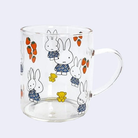 Glass mug featuring graphics of Miffy in a blue sunflower dress, strawberries and a small yellow teddy bear plush. Designs are all around the glass.