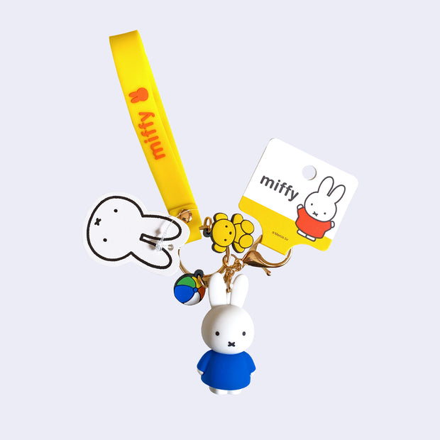 Keychain with several rubber components in addition to a lobster clasp and keychain: Miffy figure wearing a blue dress, Miffy strap, flat mini ball and flat mini teddy bear.