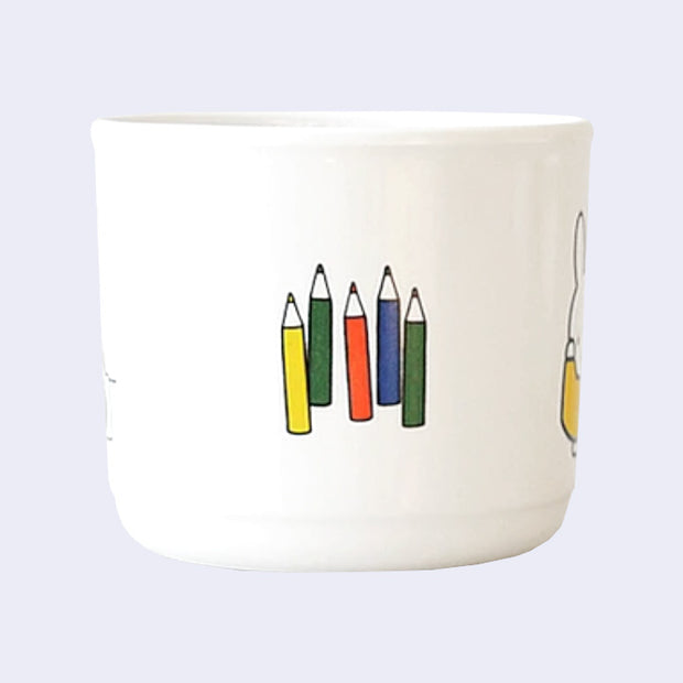 SIde view of a white melamine mug with an illustration of short sharpened colored pencils.