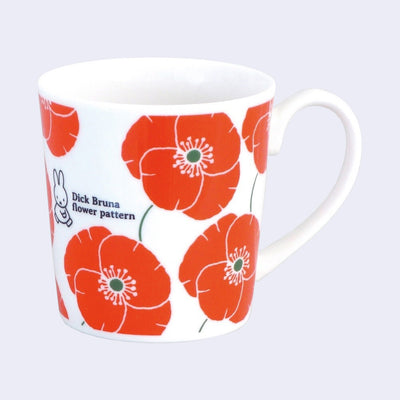 White ceramic mug featuring an orange flower pattern and a very small illustration of Miffy walking next to text that reads "Dick Bruna Flower Pattern"