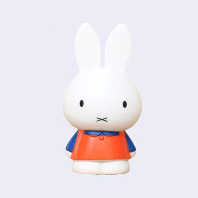 Figure of Miffy standing with her arms at her side and wearing a blue shirt under an orange dress.