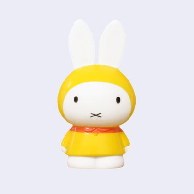 Figurine of Miffy standing with her arms at her side and wearing a yellow raincoat, with the hood on. 