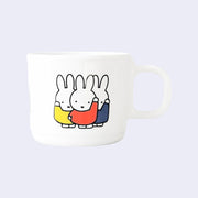 White melamine mug with a graphic of 3 Miffy characters, standing so close they slightly overlap. Each wears a different color shirt - yellow, orange and blue. 