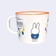 White mug with an orange rim of Miffy, standing with her arms behind her back and wearing a blue dress. Graphics on other side of the cup show several primary colored silhouettes of Miffy's head, arranged together closely like a collage.