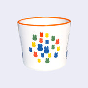 White mug with an orange rim of Miffy, standing with her arms at her sides and wearing a blue dress. Graphics on other side of the cup show several primary colored silhouettes of Miffy's head, arranged together closely like a collage.