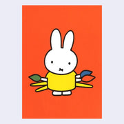 Bright orange postcard with an illustration of Miffy, wearing a yellow dress and holding 3 large paintbrushes behind her back.