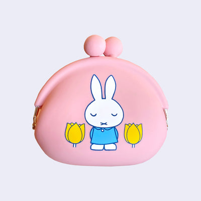 SIlicone coin pouch featuring an illustration of Miffy standing with her eyes closed and wearing a collared blue dress. She stands between 2 yellow tulip flowers.