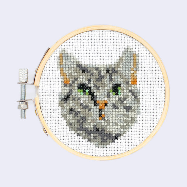 Embroidery hoop with an embroidery of a gray tabby cat's head on white background.