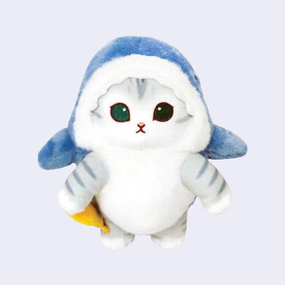 Plush doll of a gray and white cat with large teal eyes and a small mouth. It wears a blue shark costume and holds an orange squid.