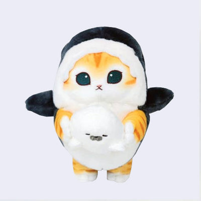 Plush doll of an orange and white cat with large teal eyes and a small mouth. It wears a dark blue shark costume and holds a sleeping white seal.