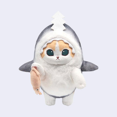 Plush doll of an orange and white cat with large teal eyes and a small mouth. It wears a gray shark costume and holds a light pink squid.