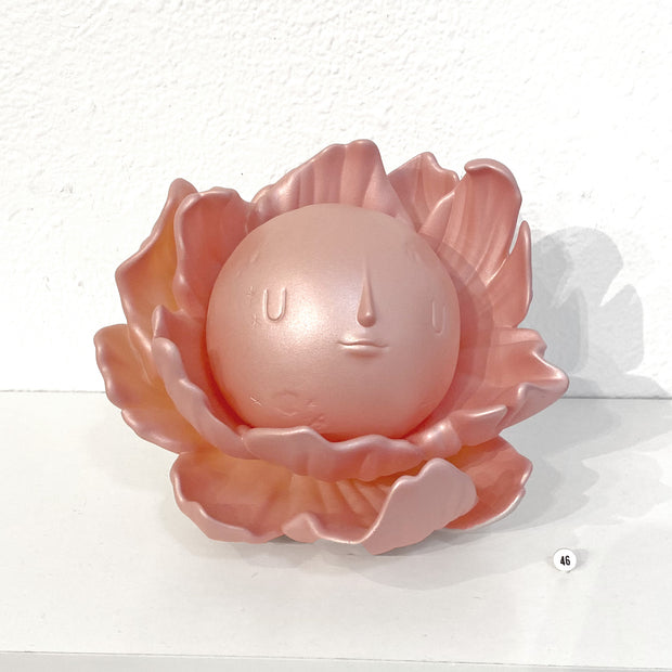 Rose gold colored vinyl figure with a glittery surface shimmer of a round full moon with a calm, minimalistic face. It sits within a series of flower petals, as if it is the pistil of the flower.