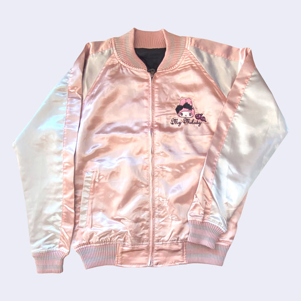 Shiny polyester bomber style jacket with a light pink body and off white sleeves. Front has a small graphic of My Melody on the left breast with her name written in white cursive below.