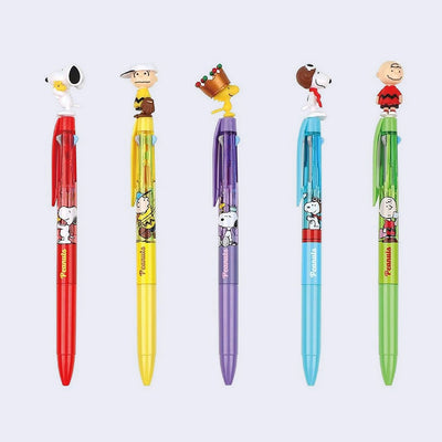 5 ballpoint pens with 3 ink channels - black, dark blue and red. Each has a colored body with a Peanuts character topping the pen.