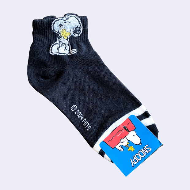 Pair of black ankle socks with ruffled cuffs. They have a graphic of Snoopy holding Woodstock to his chest.