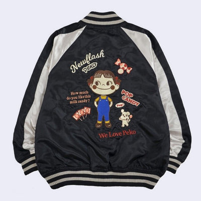 Back view of the black bomber jacket with a large embroidery of Peko Chan, a smiling girl with pigtails and overalls. Words read "Newflash Peko" and "Pop Candy" and "How much do you like this milk candy?"