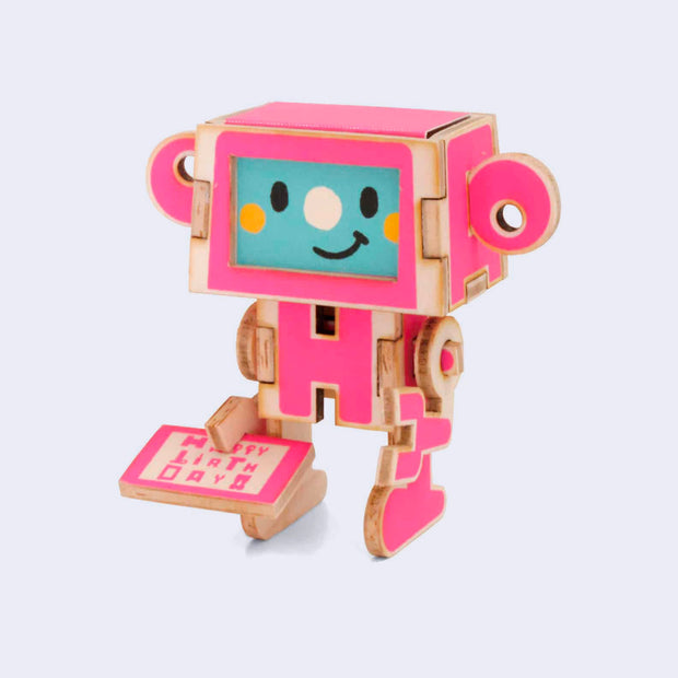 Thin wooden paper sculpture of a pink robot holding a small card that reads "happy birthday."