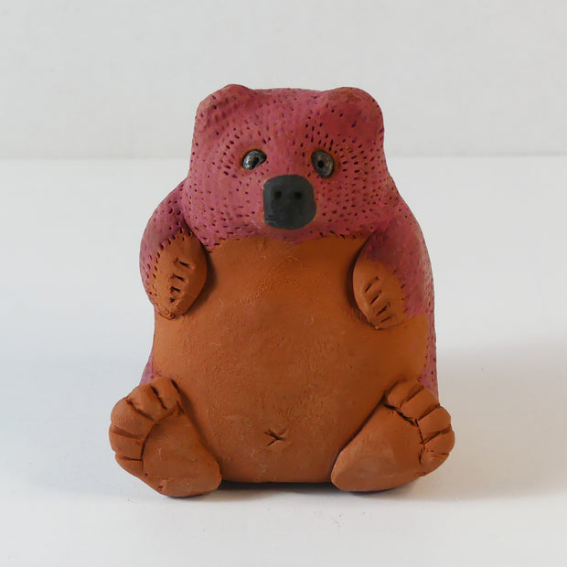 Small sculpture of a brown bear, chubby and sitting on its bottom. It has a red coloring for the top half of its body.