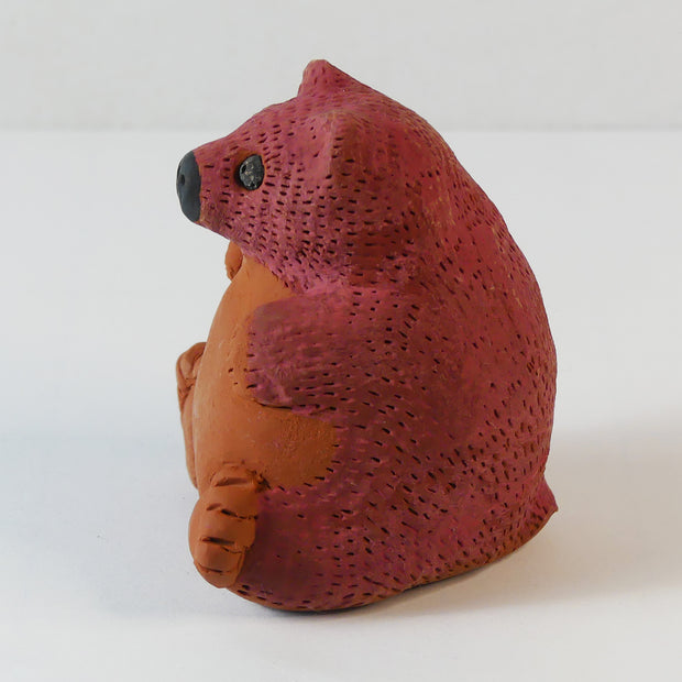 Small sculpture of a brown bear, chubby and sitting on its bottom. It has a red coloring for the top half of its body.